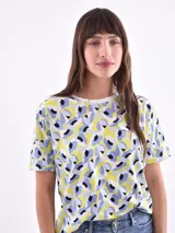 Remera de manga corta color beige con estampado de bananas en tonos amarillo, naranja y rosado.