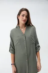 Vestido camisero verde militar, de corte recto y largo midi, con cuello mao, escote en V, cierre frontal con botones y bolsillos en el pecho. Presenta mangas largas con trabilla para sujetar arremangadas.