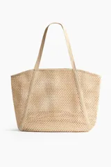 Bolso de playa de red color beige, confeccionado en paja plástica con dos asas largas y base rígida.