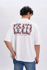 Remera blanca de manga corta y corte oversize, con estampa en la espalda en tono bordó con nombres de ciudades y texto "International vibes from the retro streets".