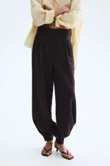 Pantalón de sarga de tiro alto color marrón oscuro, con bolsillos laterales discretos, pinzas y diseño de piernas globo con puños abotonados con frunces.