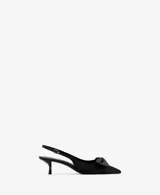 Zapato de tacón tipo slingback en color negro, con diseño destalonado, puntera fina y un detalle de lazo en la parte delantera. Cuenta con tira ajustable en el talón con hebilla metálica dorada y taco fino de altura baja.