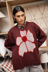 Buzo tejido de punto color bordó con diseño de flor grande en el frente, realizada en color crema con bordes y centro en relieve color rojo. Presenta cuello redondo, mangas largas y corte holgado.