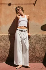 Pantalón de popelina de tiro alto y pernera ancha, de color negro. Presenta pinzas delanteras, bolsillos laterales y falsos bolsillos de vivo en la espalda. Incluye un cinturón combinado tipo pañuelo trenzado con tiras colgantes y cuentas de madera. Cierre frontal con cremallera, botón interior y gancho.