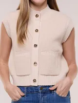 Chaleco de punto waffle color beige, con cuello medio acanalado, abotonadura frontal con botones metálicos dorados y bolsillos frontales aplicados.