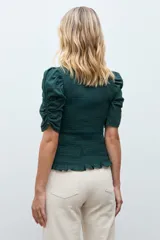 Blusa de color gris oscuro con diseño de punto smock en el cuerpo, cuello redondo y mangas cortas abullonadas con detalle de volados en el ruedo.