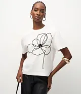 Remera de corte box, levemente amplia, confeccionada en algodón. Presenta cuello redondo, mangas cortas y un diseño de flor bordada en hilo negro en la parte delantera.