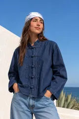 Chaqueta de jean azul oscuro con cuello mao y cierre frontal con nudos chinos o de estilo japonés.