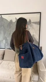 Bolso de mano tipo duffel color azul marino, de gran capacidad, con asas de cuero marrón y correa ajustable para hombro o cruzada.
