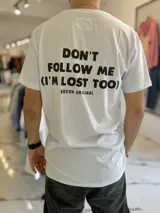 Remera blanca de manga corta con estampa frontal y de texto grande en la espalda que dice 'DON'T FOLLOW ME (I'M LOST TOO)' y la marca 'DUXON ORIGINAL'.