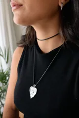 Collar con dije de corazón en acero quirúrgico, con textura irregular y relieve, montado sobre un tiento encerado negro.