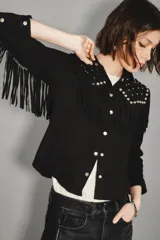 Camisa negra de gamuza caprina con cuello y hombros adornados con tachas metálicas plateadas. Presenta flecos decorativos en el canesú y botones plateados en el frente.