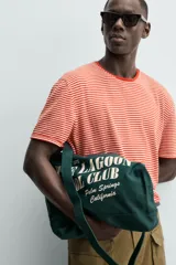 Bolso tipo shopper de algodón en color verde oscuro, con diseño de estampado tipográfico en color crema en el frente. Cuenta con dos asas de mano y cierre magnético.