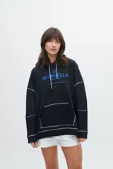 Canguro color crudo con capucha, cordón de ajuste celeste, bolsillo tipo canguro, puños y ruedo acanalados, y estampado frontal con la frase "The Seashells".