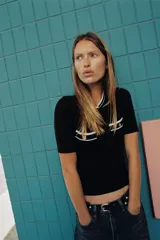 Camiseta negra de manga corta y corte slim fit, con cuello redondo ribeteado en blanco y dos bolsillos de plastrón en el pecho con un botón dorado cada uno.