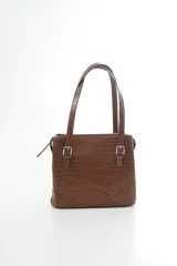 Cartera de hombro estructurada color negro, confeccionada en 100% cuero vacuno con textura en relieve tipo reptil. Cuenta con asas largas ajustables mediante hebillas metálicas plateadas, cierre superior y el logo de la marca grabado en la parte frontal.