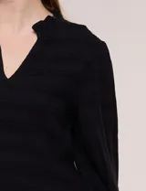 Blusa negra de rayón con textura smock en la pechera, escote en V con cuello mao fruncido, mangas largas fluidas con puños anchos y detalle de volados en el ruedo.