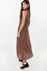 Vestido midi marrón de lino italiano, con cuello halter, sin mangas y diseño asimétrico con volados en el ruedo.