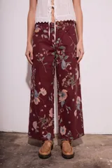 Jean de corte wide leg con tiro medio, confeccionado en algodón peinado. Presenta un diseño estampado con motivos florales sobre una base de color bordó.