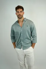 Camisa de manga larga en color verde agua, confeccionada en tejido de lino con textura sutil. Presenta cuello camisero con botones, cierre frontal abotonado y un pequeño logo bordado en el pecho.