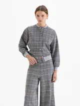 Buzo tipo bomber de tela de punto con estampado de cuadros, cuello redondo, puños y ruedo tejidos en color gris. Presenta cierre frontal con broches a presión y mangas largas con diseño holgado.