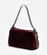Cartera mediana de pelo sintético color bordó, con asa única de cuero sintético brillante, cierre superior por cremallera y detalles de argollas metálicas en los laterales.
