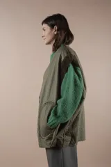 Chaleco largo acolchado color verde oliva, reversible con un lado de piel sintética y otro de pelo sintético. Tiene cuello en V, cierre con botones a presión y bolsillos laterales. Silueta amplia y relajada.