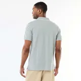 Chomba de piqué color gris melange, con cuello polo y cierre frontal de tres botones. Presenta detalles de líneas blancas en el borde del cuello y de las mangas, y un sutil bordado al tono en el pecho.