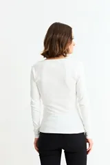 Remera de manga larga, color blanco, con tejido acanalado y escote cuadrado. Presenta un cierre metálico dorado en el centro del escote.