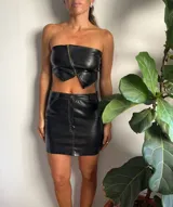 Minifalda negra de cuero sintético con bolsillos traseros y costuras blancas contrastantes.