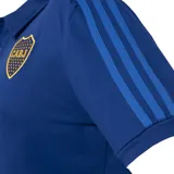 Chomba azul con cuello clásico y tapeta de botones. Presenta las tres tiras características de Adidas en los hombros y el logo de la marca bordado en dorado en el pecho. También incluye el escudo del club Boca Juniors bordado en el pecho.