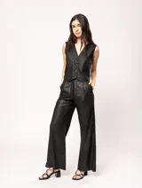 Pantalón de lino color beige, de tiro alto, pierna ancha y levemente acampanada. Tiene pinzas delanteras, elástico en la pretina trasera, cierre delantero y broche interno, bolsillos laterales y dobladillo invisible.