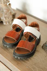 Sandalias de cuero color marrón con textura de cocodrilo, suela track color negro, tira ancha blanca y ajuste con hebilla.