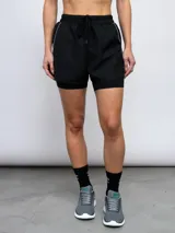 Short de entrenamiento Umbro de mujer, color negro, confeccionado en poliéster con calza interna incorporada. Cuenta con cintura elástica ajustable con cordón y detalles de ribetes reflectivos.