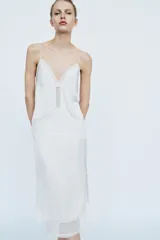 Falda midi de tiro medio, color blanco, confeccionada en hilatura de viscosa 100%, con detalle de aplicación de tejido combinado semitransparente con abertura en el bajo y cierre lateral con cremallera oculta.