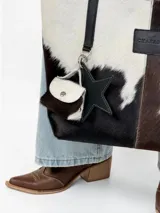 Cartera tote de cuero con pelo vacuno en tonos blanco y negro, con asas largas de hombro, parche frontal con logo y charms colgantes en forma de estrella y mini monedero.