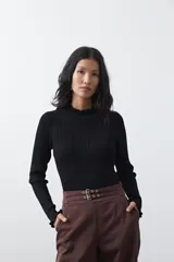 Polera de tejido acanalado color negro, con cuello alto y puños con terminación de volados. Presenta un diseño entallado y textura vertical.