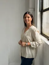 Blusa de lino color beige con cuello en V, cierre frontal con botones y mangas largas con sutil fruncido en los hombros.