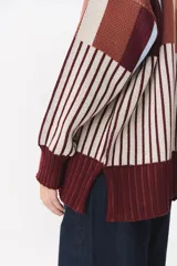 Buzo oversize de tejido de punto con diseño de bloques y rayas verticales en colores rojo, verde, bordó y crema. Presenta cuello alto tejido y terminaciones en rib en puños y ruedo.