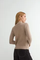 Buzo de punto color crema con cuello alto, manga larga y puños y ruedo acanalados.