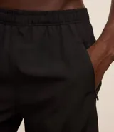 Bermuda deportiva gris con cintura elástica, cordón de ajuste, bolsillos con cremallera, recorte lateral con agujeritos y abertura en el bajo.