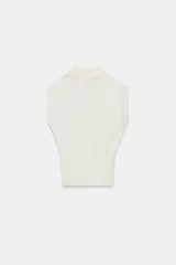 Chaleco de punto color blanco, estilo polo, sin mangas (manga sisa) y cuello solapa. La parte inferior termina en rib.