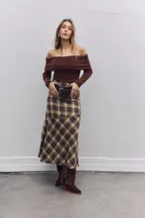 Falda midi de corte evasé con estampado de cuadros escoceses en tonos marrones y beige. Presenta un diseño asimétrico en el ruedo y cierre lateral.