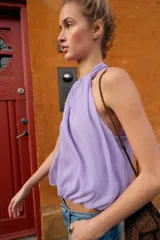 Top corto de cuello halter con diseño delantero cruzado y bajo abullonado con elástico. Presenta un estampado sutil de lunares y cierre en la espalda con botones ocultos.