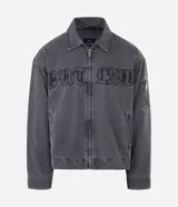 Chaqueta de denim color gris con acabado estonado, cierre frontal con cremallera, cuello camisero y manga larga. Presenta un estampado con la palabra 'OUTLAW' en tipografía gótica en el pecho y un bolsillo con cierre en la manga izquierda.