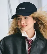 Gorra de sarga color negro con visera curva y bordado frontal en blanco con la frase "NOT YOUR BABE". Cuenta con regulador en la parte trasera.