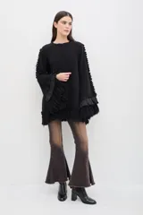 Sweater negro de lana merino con silueta amplia y relajada. Presenta mangas acampanadas con volumen, decoradas con volados de lino y terminaciones de flecos en los puños y en el ruedo.