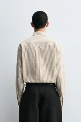 Camisa de corte relajado confeccionada en algodón, con estampado de rayas verticales. Presenta cuello solapa, manga larga con puños abotonados, bolsillo frontal y corbata integrada del mismo tejido.