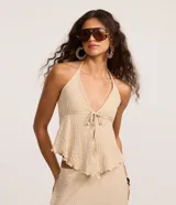 Blusa beige texturizada de corte halter con escote en V, lazo frontal ajustable en el busto y ruedo asimétrico ondulado.