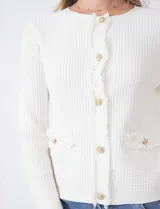 Cardigan de punto color fucsia, con escote a la base, cierre frontal con botones metálicos dorados y terminaciones desflecadas. Presenta bolsillos simulados en la parte delantera y mangas largas.